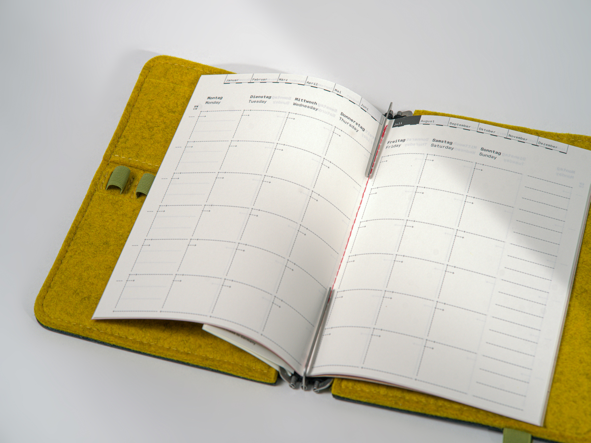 Undated monthly planner in M size (14 × 20 cm) for A5, sewn with red thread, featuring a sturdy cover made from recycled cardboard. 32 pages with colored endpapers.